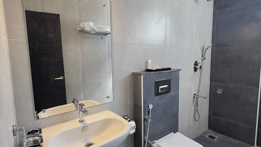 A bathroom with a wash basin under a mirror, a water heater fixed on the wall, and a toilet beside it.