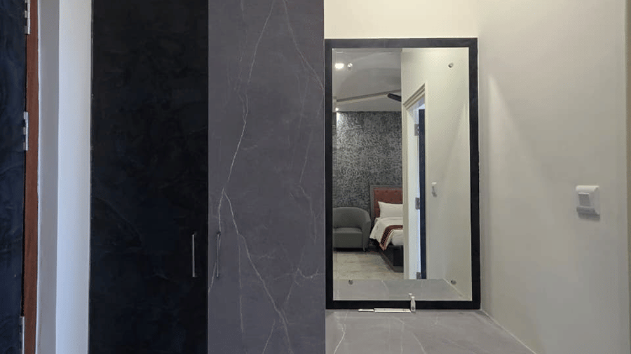 A dressing space with a dark wooden wardrobe, a wall mirror, and a small stool nearby.