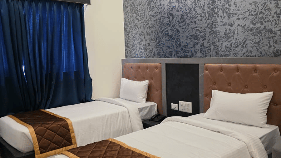 Two single beds placed side by side, set against a dark patterned accent wall with blue curtains