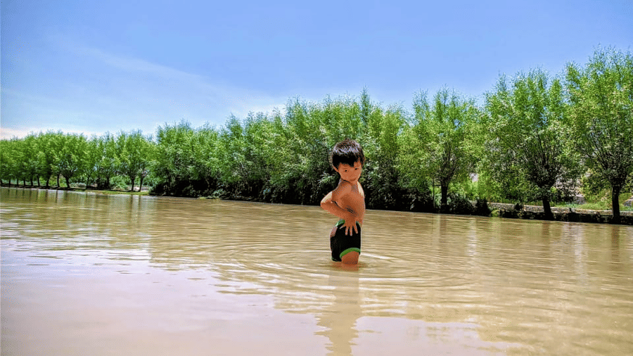 A person wading through the middle of a wide, calm river flanked by trees at Indus Serenity Retreat.