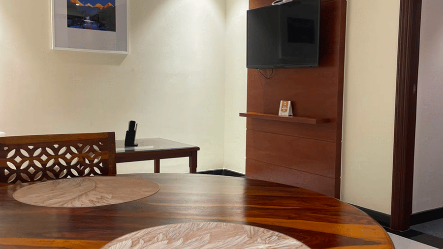 A dining area with a table, chairs, and a wall mounted frame and a television in the backdrop. | MM Legacy, Kanchipuram