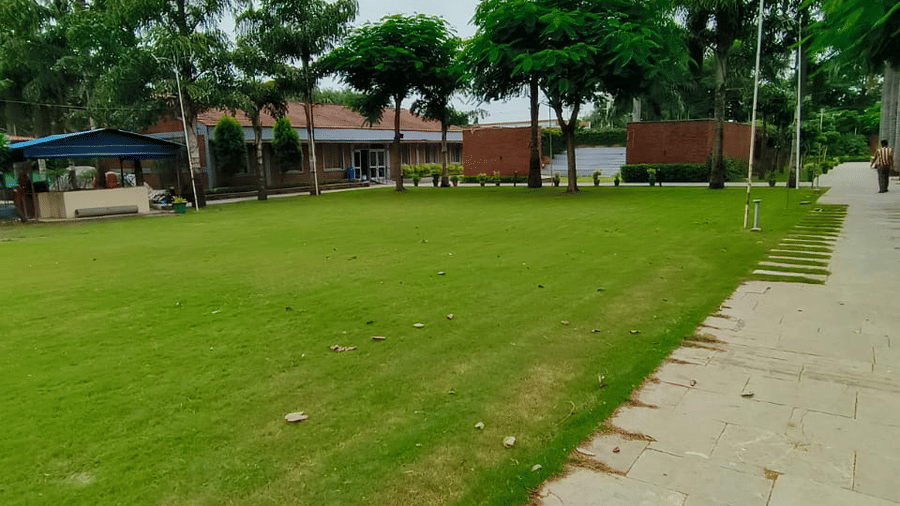 A wide expanse of green lawn next to a stone path under a mostly cloudy sky, with some low buildings and trees visible in the distance | Nandan Resort