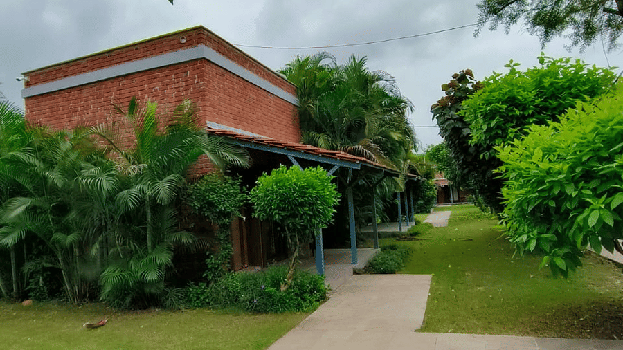 A view of a well-maintained lawn and a red brick building partially visible through the trees on a cloudy day | Nandan Resort