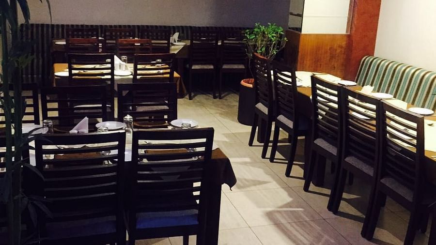 A restaurant dining room with striped bench seating, wooden chairs and decorative wall plates - TGI Apple Inn, Jaipur 