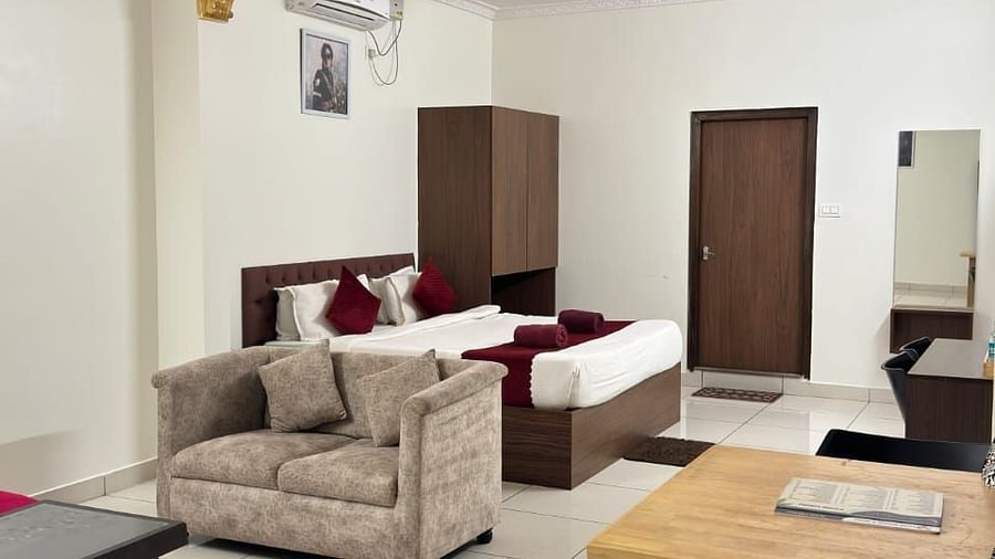 Modern living area with a beige sofa, red armchair, glass coffee table, and a plush bed in the background. | Vistar Resort, Bengaluru