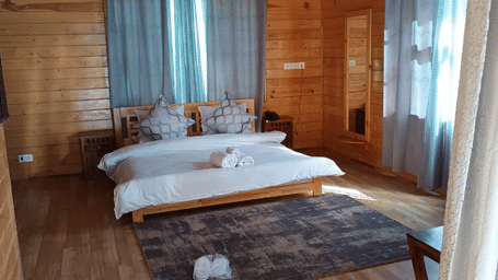 A Deluxe Room With Bathtub bedroom at Dawat e Drung by FrozenFall Resort, Drung, Tangmarg, featuring a double bed on a wooden floor next to a floor rug.