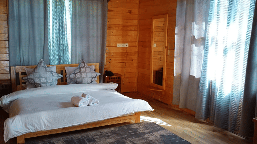 A wood-panelled bedroom at Dawat e Drung by FrozenFall Resort, Drung, Tangmarg, featuring 1 double bed, a floor rug and window curtains.