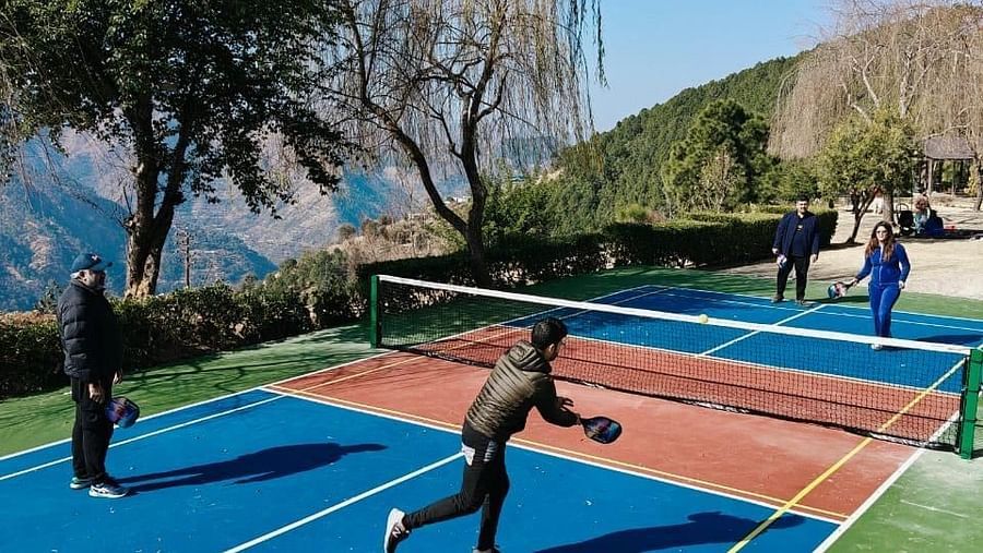Guests playing pickle ball on vibrant blue and red court surrounded by mountain scenery and lush gardens at The Manor Wellness & Sports Hotel
