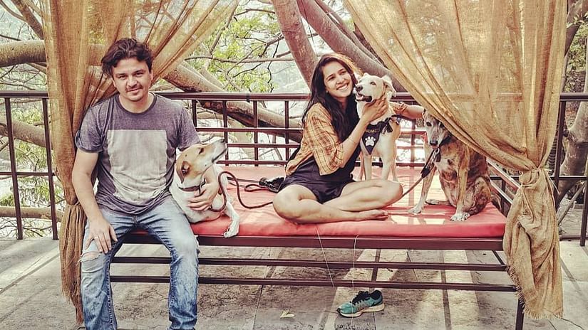a guy and a girl sitting on a swing with a dog beside them