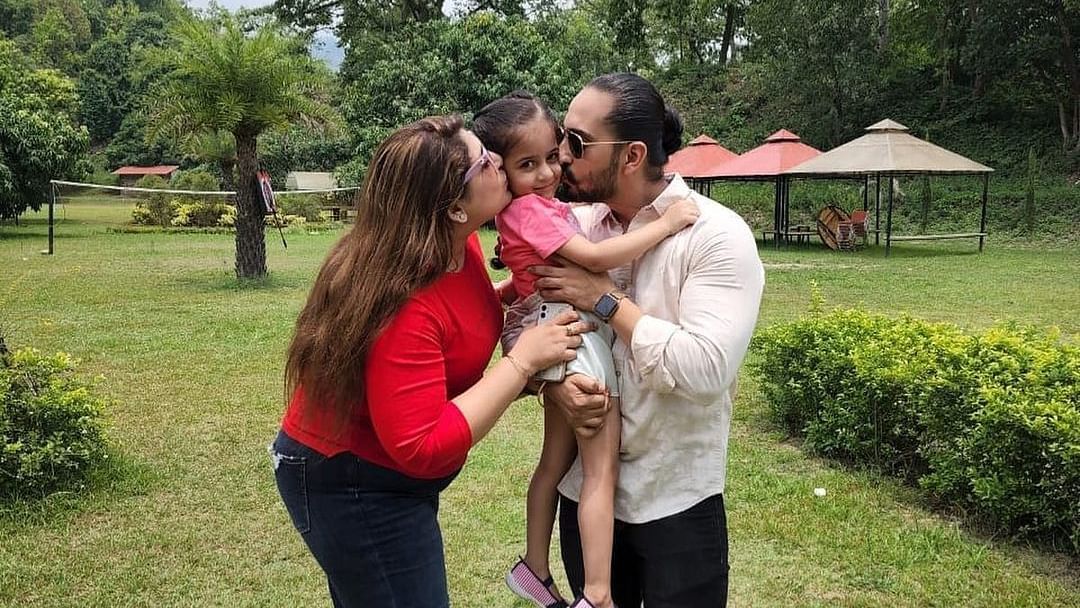 A couple kissing a child in a lawn on a sunny day at The Sylvan Retreat, Dehradun.