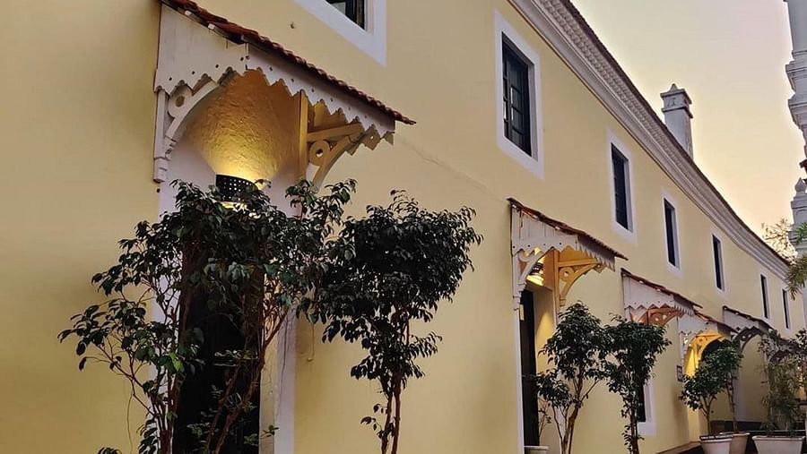 A cream-colored building with dark windows and doors, possibly part of a hotel or resort, with potted plants lining a walkway at Fort Tiracol, Goa.