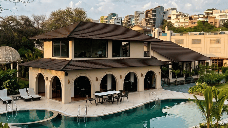 Outdoor swimming pool beside multi storey building with arched openings, sun loungers, dining table, and palm trees at Jivana Wellness Retreat.