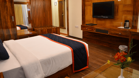 Executive Room with a king bed, warm wooden interiors, and a flat-screen TV at Benzz Park, offering a cozy and comfortable stay for guests.