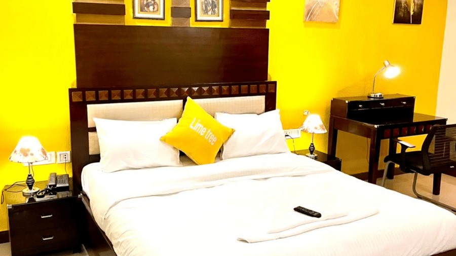 Bedroom of Lime Tree Hotels & Service Apartment Private Limited featuring a yellow cushion, a work desk, and framed wall art.