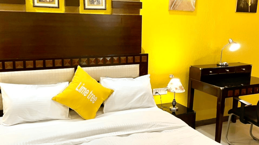 Bedroom of Lime Tree Hotels & Service Apartment Private Limited featuring a yellow throw pillow, a work desk, and framed wall art.