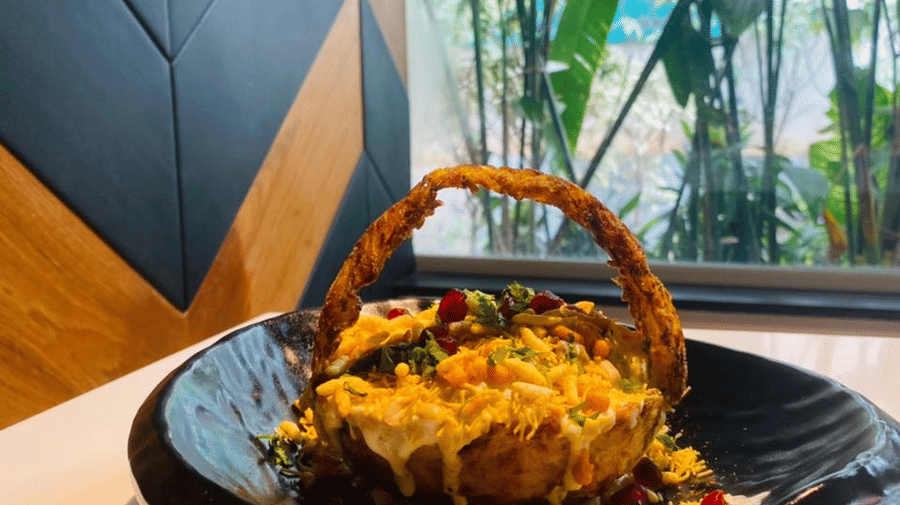 Chaat basket at The Citrine, Bangalore, plated in a dark bowl, topped with sev-pomegranate, and a Citrine signboard visible through the window.