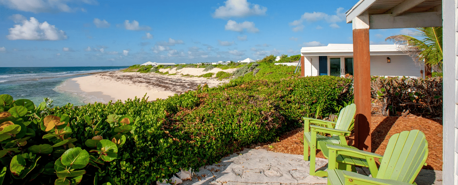 Patio with green chairs facing the ocean and coastal vegetation | Abaco Inn