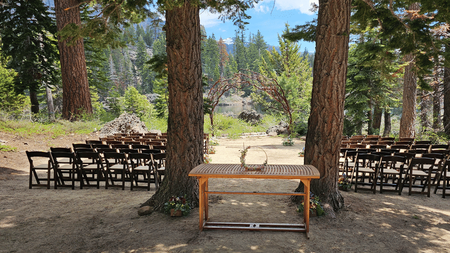A serene outdoor ceremony space at Kit Carson Lodge with rows of chairs facing a simple wooden table framed by 2 large pine trees and mountain views in the distance