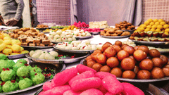 A street food scene with many sweets kept on large plates for people to buy