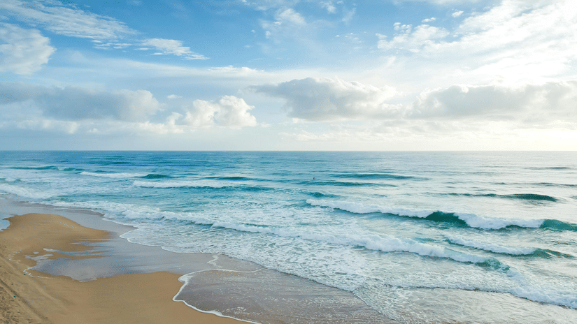 image of a clear beach side with blue sea waves crashing on the shoreline