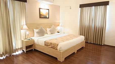Plush bed on a well-furnished floor under warm lighting with two lamps on the nightstands on both sides of the bed inside premium studio at Starlit Suites, Shirdi
