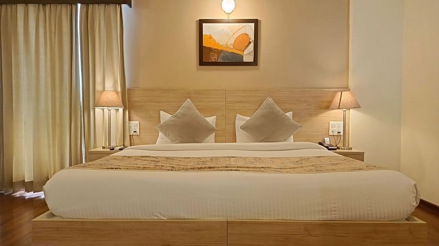 Premium Studio at Starlit Suites, Shirdi features a large double bed with neutral-toned bedding and cushions, bedside tables with lamps, and light-coloured curtains.