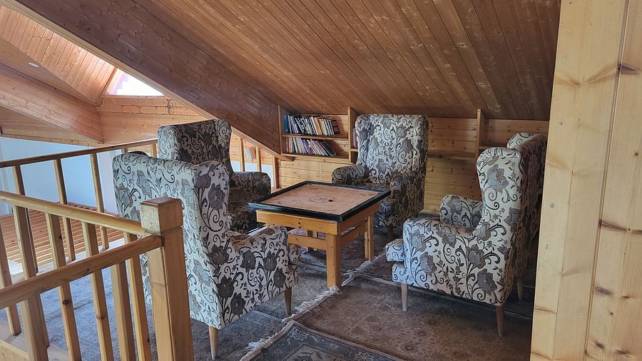 Wooden loft indoor area with upholstered chairs and books arranged at the back in a shelf at Dagshai Manor Kasauli - Inde Hotels