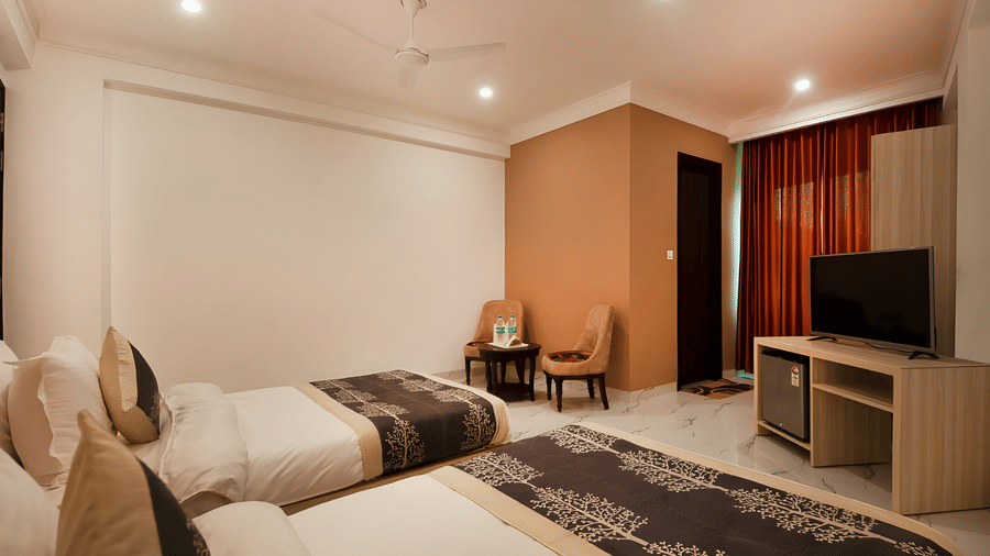 A twin room at Hotel Apple Park Delhi with warm ambient lighting, featuring beds with dark patterned runners and a television unit with a built-in mini-fridge.