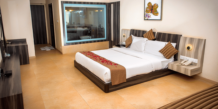 A view of the bed in Regency Room with its two side tables, glass window to the bathroom, diwan, and a consoel.