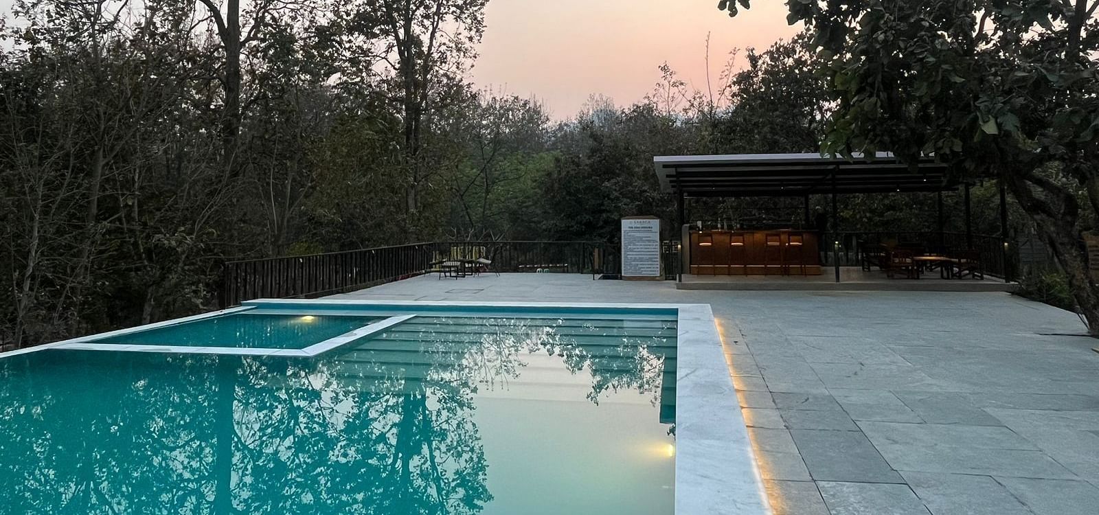 Outdoor swimming pool at Saraca Resort & Spa Corbett surrounded by trees at evening