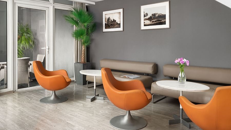 A chic lounge area at The Atara, Gurugram offering a variety of seating, including unique armchairs and a sofa, with a large glass door providing seamless access to an adjacent outdoor balcony