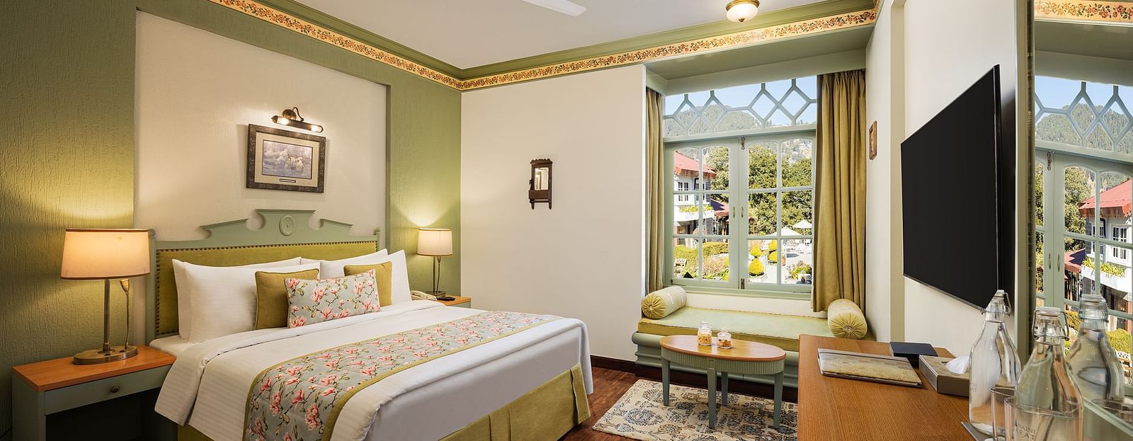 An image of a  cozy room in the naini retreat, nainital, with a king-size bed, wooden furniture, and a window. The room also features a ceiling fan, a TV and wooden flooring.