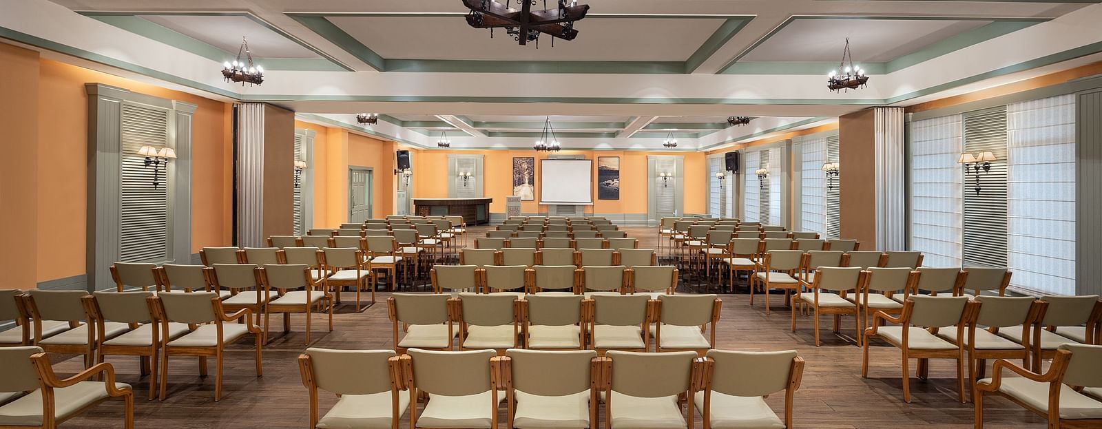 An image of a conference hall with a set of table and chairs in each corner and a projector screen at the front of the room - The Riverview Retreat, Corbett
