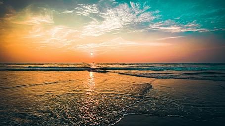 an overview of a beach in goa with the sun setting while creating different hues in the sky.