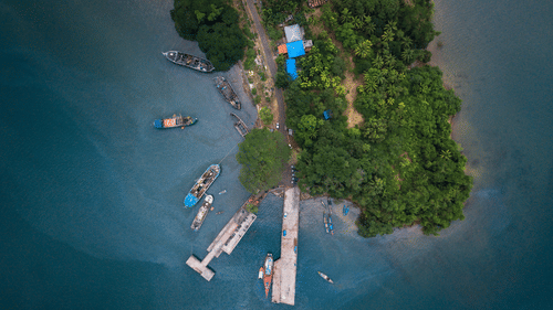 Aerial view of a port with ships docking on the side surrounded by lush greenery.