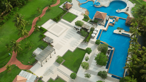 An aerial view of Kenilworth Resort & Spa, Goa, with the different rooms, lawn area, trees, walking pathway, and the swimming pool in view.