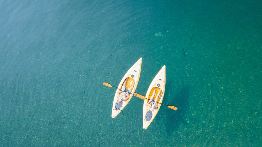 Two kayaks with people paddling on clear waters.