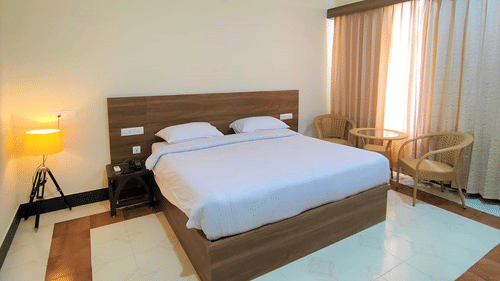 Room at Pride Resort Rudraprayag featuring a double bed with a wooden headboard with a floor lamp in the corner and a sitting space right next to the window