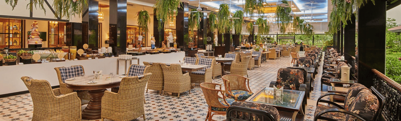 Spacious, elegant restaurant with a high ceiling, hanging greenery, comfortable neutral-toned seating, and a decorative patterned floor.
