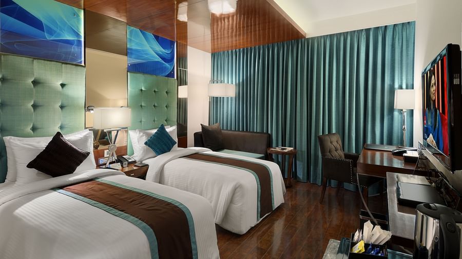 Elegant room with twin beds, velvet curtains, and plush seating at The Elanza Hotel.
