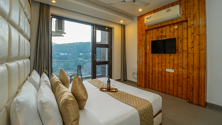 An image of the premium room with a bed, flat screen TV, and a glass door leading to the balcony overlooking the view - DLS Whispering Winds