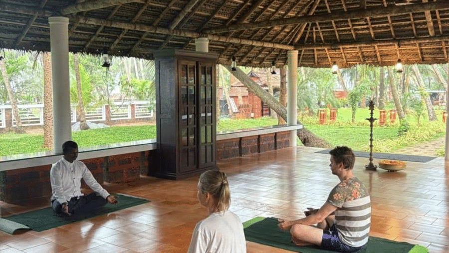 Over-view of people practicing yoga postures on mats in a tranquil, open-air setting with a thatched roof  at Ayur On The Beach Nattika.