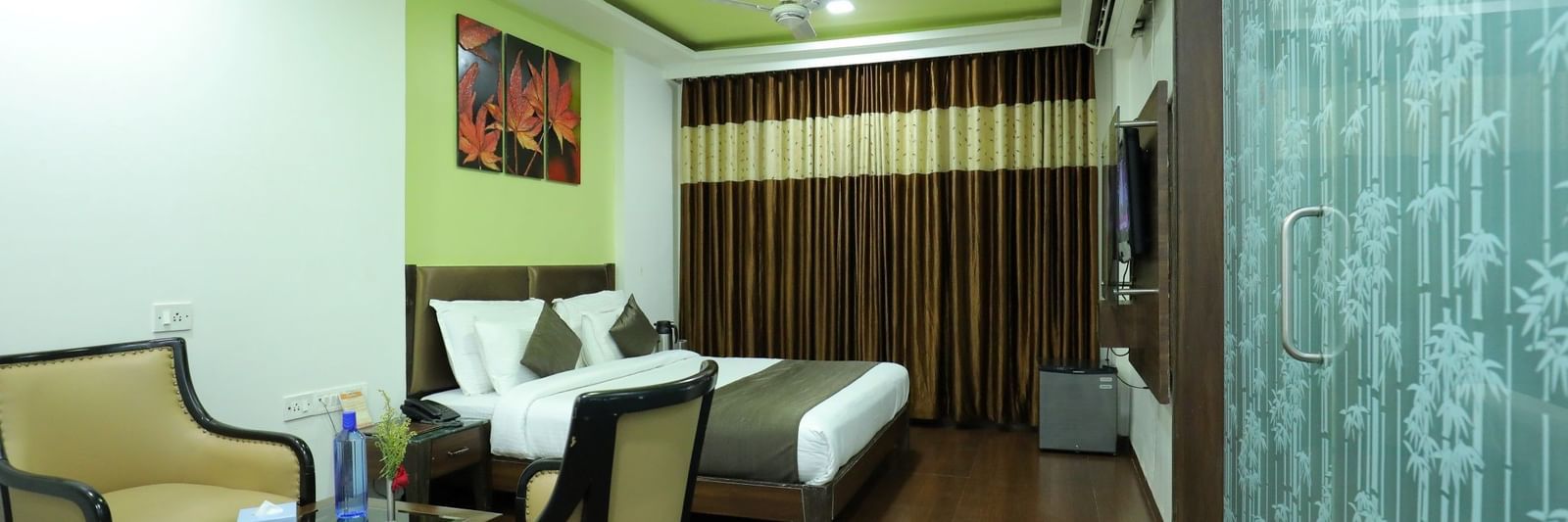 A bedroom at Krushnai Resort with a bed, 2 chairs, a glass parting on one side, and a vibrant green ceiling.