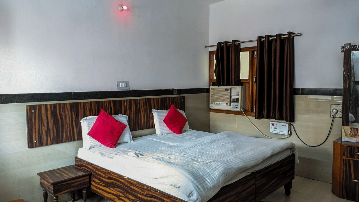 Double bed in the room with pillows and cushions and a nightstand - Hotel Goverdhan, Agra