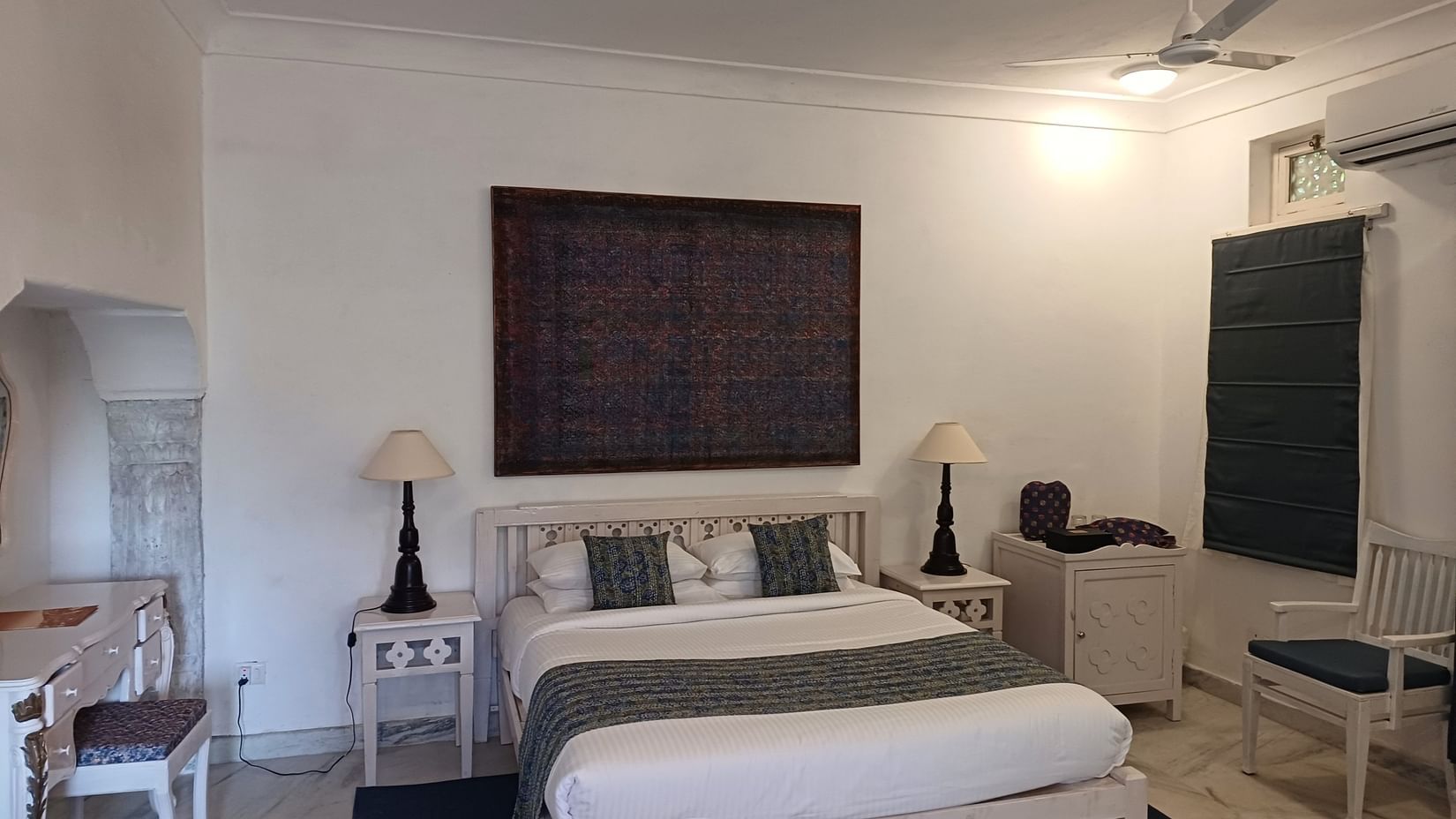 Well-appointed room featuring dark artwork, white wooden bed, matching nightstands, and dual table lamps at Neemrana Fort-Palace - 15th Century, Delhi-Jaipur Highway.