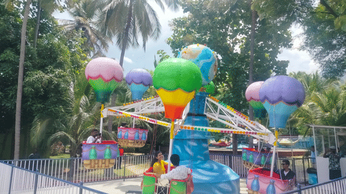 A colourful hot air balloon-themed ride at Black Thunder, Coimbatore with a couple enjoying the ride, surrounded by trees.