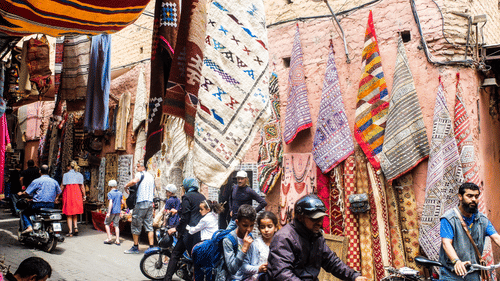 Bustling market street with colourful fabrics and busy crowd.