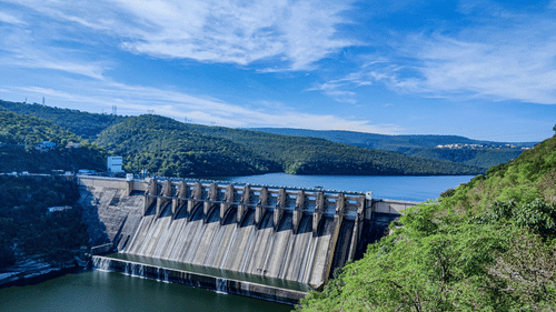 a water dam surrounded by lush green mountains and blue sky in the background.