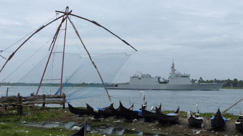 Chinese fishing nets under a cloudy sky in Fort Kochi with boats lined up and a ship sailing on the water