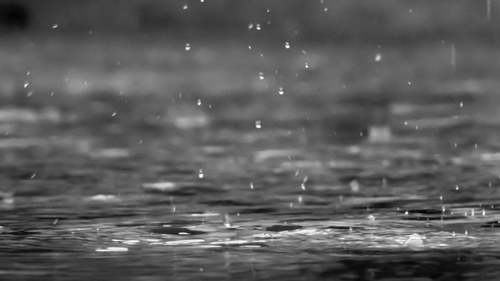 A close up shot of rain droplets falling on the floor with water on the floor